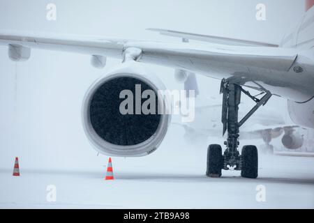 Verkehr am Flughafen bei starkem Schneefall. Schneeflocken gegen Düsentriebwerk und Rollflugzeug auf dem Rollweg des Flughafens an frostigen Wintertagen. Extremer Witterungseinfluss Stockfoto