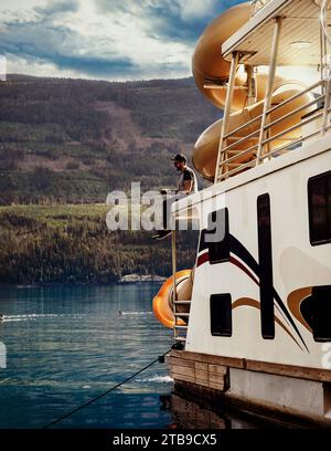 Mann genießt ein Hausboot, Familienurlaub und Angeln von Deck, während er am Ufer des Shuswap Lake parkt Stockfoto