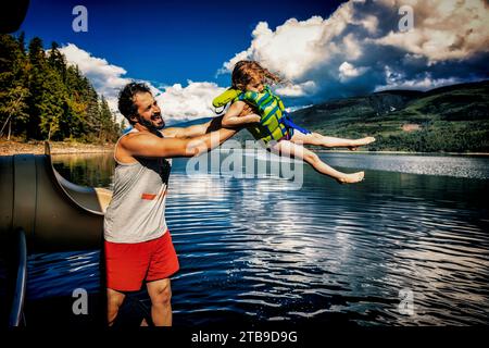 Mann, der vorgibt, ein junges Mädchen aus einem Hausboot ins Wasser zu werfen, während eine Familie einen Urlaub am Shuswap Lake, British Columbia, Kanada, genießt Stockfoto