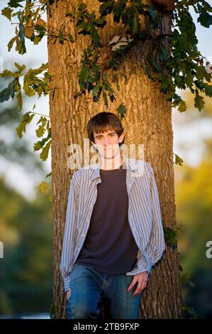 Außenporträt eines Teenagers, der sich auf einen Baum lehnt; Lincoln, Nebraska, Vereinigte Staaten von Amerika Stockfoto