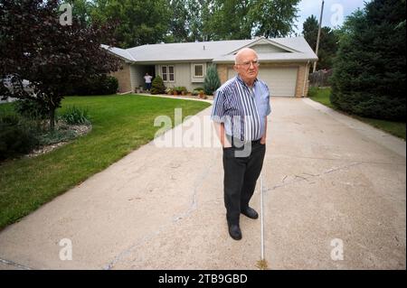 Ein älterer Mann steht in der Einfahrt seines Hauses, seine Frau steht an der vorderen Tür und läuft die Distanz; Elkhorn, Nebraska, Vereinigte Staaten von Amerika Stockfoto