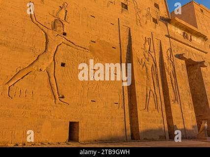 Nahaufnahme des Flachreliefs auf dem beeindruckenden Eingangspylon des Tempels des Horus in goldenem Licht; Edfu, Ägypten, Nordafrika Stockfoto