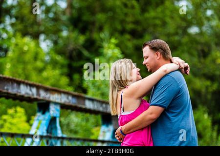 Porträt eines Paares, das auf einer hölzernen Brücke steht und sich umhüllt und ansieht, während er in einem Park spaziert Stockfoto