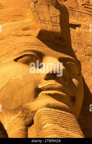 Nahaufnahme einer der Ramses II-Statuen, die aus dem Berghang vor dem Großen Sonnentempel von Abu Simbel mit goldenem Licht gemeißelt wurden Stockfoto