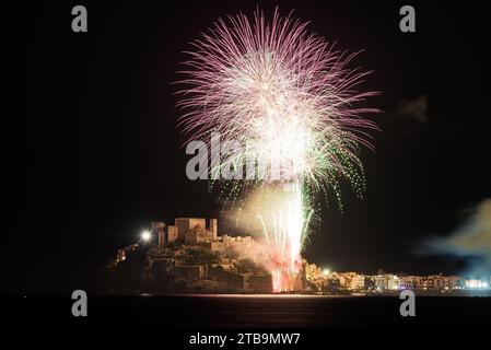 Ein atemberaubendes nächtliches Foto des Dorfes Peñiscola mit der Burg, den Häusern und dem Palmenfeuerwerk in verschiedenen Farben, das goldene, mit Witz festgehaltene Feuerwerk Stockfoto