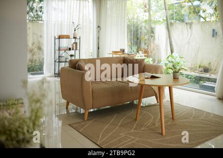 Gemütliches Sofa neben einem kleinen Couchtisch mit offenem Buch und einer Tasse Tee Stockfoto