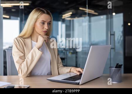 Eine umsichtige und ernsthafte Geschäftsfrau sitzt im Büro am Tisch und konzentriert sich auf die Arbeit am Laptop. Stockfoto