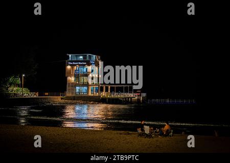 Eine Gruppe von Leuten, die eine Nacht am Strand genossen, versammelte sich um die Küste in der Nähe des glitzernden Wassers des Ozeans Stockfoto