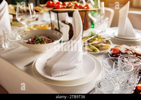 Festliches Servieren, Tischdecken. Teller dekoriert weiße Serviette, Besteck, leere Kristallweingläser und verschiedene leckere Mahlzeiten. Hochzeitsvorbereitungen, Abendessen Ta Stockfoto