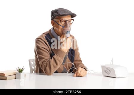 Älterer Mann, der auf einem Tisch sitzt und einen Vernebler benutzt, der auf weißem Hintergrund isoliert ist Stockfoto