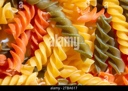 Ungekochte Fusilli Pasta in leuchtenden Farben: Eine faszinierende kulinarische Leinwand aus bunten Spiralen, die einen lebendigen und strukturierten Hintergrund für Gourmet-Kochen schafft. Farbige Trockene Pasta. Rohe Makkaroni Stockfoto