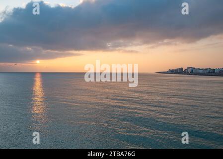 Ein Sonnenuntergang im frühen Winter über dem Meer mit Worthing Promenade (Mitte rechts) - Worthing, West Sussex, Südengland, Großbritannien. Stockfoto