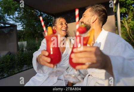 Paare in weißen Bademänteln, die draußen im Spa Resort mit roten Cocktails locken Stockfoto