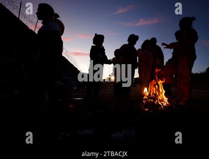 Jacumba Hot Springs, Kalifornien, USA. Dezember 2023. Eine Asylsuchende Migrantenfamilie mit kleinen Kindern aus Columbia versucht, sich neben einem Feuer in einem Freiluftlager an der Grenze zwischen den USA und Mexiko in der Nähe der kleinen Wüstengemeinde Jacumba Hot Springs im San Diego County warm zu halten. Hunderte von Asylbewerbern überqueren täglich die Grenze in die Vereinigten Staaten und erleben kalte Nächte, in denen sie auf ihre Bearbeitung warten. (Kreditbild: © K.C. Alfred/ZUMA Press Wire) NUR REDAKTIONELLE VERWENDUNG! Nicht für kommerzielle ZWECKE! Stockfoto