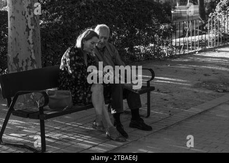 Mann und Frau im Alter, die auf ein Smartphone schauen, sitzen auf einer Bank im Parque de La Montaña in Madrid, Sapin Stockfoto