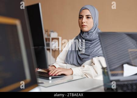 Porträt einer selbstbewussten muslimischen Frau als Softwareprogrammiererin, die im Büro am Computer arbeitet Stockfoto