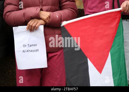 London, Großbritannien. Dezember 2023. Ein Demonstrant hält ein Schild mit dem Namen Dr. Tamer Al-Khayyat auf, während ein anderer während einer Demonstration vor dem St. Thomas's Hospital die palästinensische Flagge hält. Gesundheitspersonal versammeln sich vor ihrem Krankenhaus, St. Thomas, um Kollegen hervorzuheben, die während des Krieges im Gazastreifen gestorben oder vermisst wurden. Sie fordern einen dauerhaften Waffenstillstand. Quelle: SOPA Images Limited/Alamy Live News Stockfoto