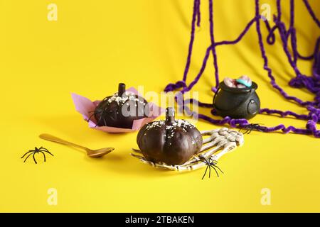 Köstliche Schokoladenkuchen, Skelett Hand und Spinnen für Halloween Feier auf gelbem Hintergrund Stockfoto