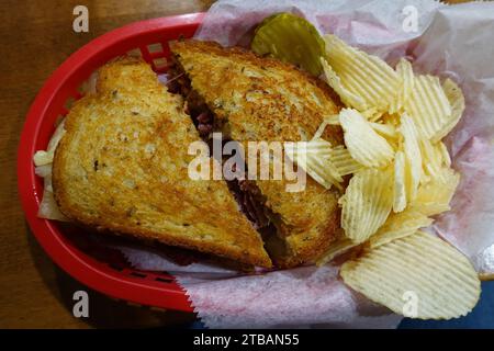 Ein klassisches Reuben-Sandwich, serviert in einem Korb mit Kartoffelchips und Gurken aus Corned Beef, Sauerkraut, schweizer Käse und Spezialsauce. Stockfoto