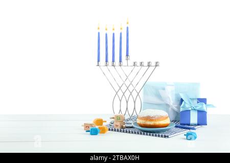 Hanukkah-Feier. Komposition mit Menora, Dreidels und Donut auf Tisch vor weißem Hintergrund Stockfoto