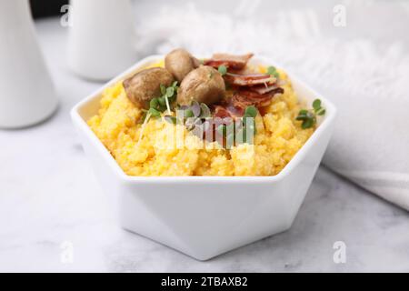 Gekochtes Maismehl mit Speck, Pilzen und Mikrogrün in Schüssel auf weißem Marmortisch, Nahaufnahme Stockfoto