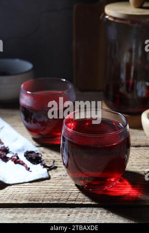 Köstlicher Hibiskus-Tee in Tassen und trockene roselblätter auf Holztisch Stockfoto