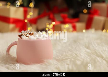 Weihnachtskakao mit Marshmallows und Lebkuchenkeks in rosa Tasse auf weichem Teppich drinnen, Nahaufnahme. Leerzeichen für Text Stockfoto