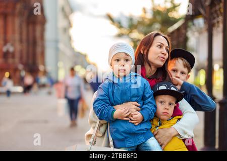 Die viel beschäftigte Mutter mit Kindergruppe steht auf der Stadtstraße. Frau und süße Söhne spazieren gern auf dem Marktplatz. Große glückliche Familie mit Kindern Stockfoto