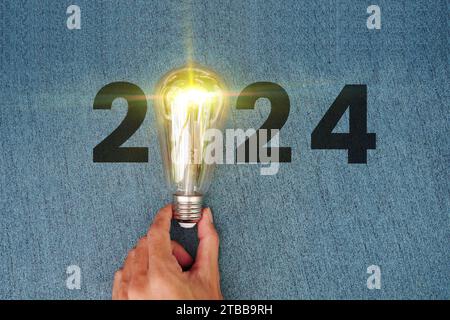 Grußkarte für das neue Jahr 2024 mit Glühbirnen. Leuchtender Kalender 2024, kreative Trendlampe, die von Geschäftsmanns Hand gehalten wird und leuchtend leuchtet. Stockfoto