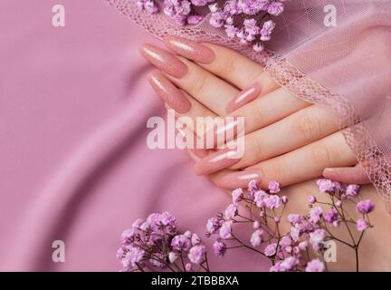 Weibliche Hände mit schöner Maniküre mit Gipsofila-Blüten auf rosa Seide Stockfoto