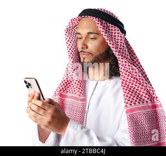 Junger arabischer Mann in traditioneller Kleidung, der ein Smartphone auf weißem Hintergrund benutzt Stockfoto