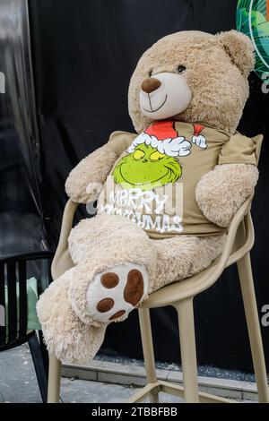 Lustiger Bär zu Weihnachten gekleidet mit dem Grinch Merry Christmas T-Shirt auf einem Stuhl Stockfoto