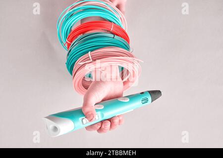 Kinderhand mit modernem 3D-Stift und bunten Plastikschnüren auf der Hand. Hobby-, Spielzeug- und Bastelhintergründe Stockfoto