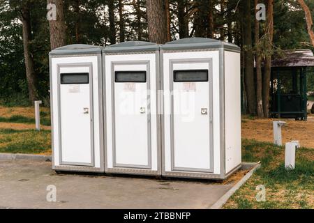 Eine Reihe von tragbaren Toiletten, die in einer Veranstaltung oder einem Park im Freien angeordnet sind. Die Kabinen sind in hellen Farben gehalten und verfügen über offene Türen, die von einem verwendet werden können Stockfoto