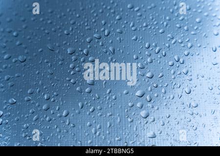 Nahaufnahme von Regentropfen auf einem Fensterglas mit Stadtlichtern, die an einem regnerischen Abend im Hintergrund reflektieren, was eine ruhige und fesselnde Stadt schafft Stockfoto