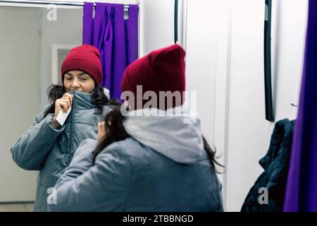 Eine Frau mittleren Alters probiert Jacke und Hut in der Garderobe der Abholstelle an Stockfoto