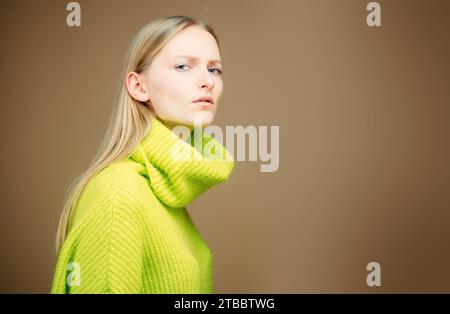 Nahaufnahme attraktive europäische blonde Frau mit langen Haaren, geneigtem Kopf, in einer halben Drehung stehend, in lässigem grünen Outfit. Verdächtiges Ansehen und Zuhören Stockfoto