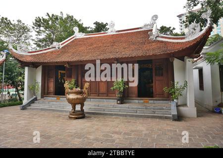 Außenansicht eines buddhistischen Tempels mit Pagodendach aus Lehm und weißen Drachenskulpturen auf den Graten. Eine große bronzene Räucherurne sitzt vorne Stockfoto