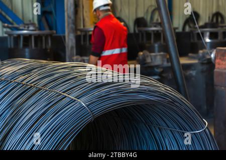 Arbeiter oder Mann mit Spulen aus Eisen- oder Stahldraht, die in der Metallindustrie gestapelt sind. Bauindustrie Stahlwerk Konzept Bild Stockfoto