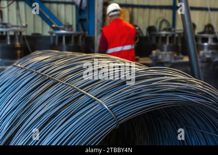 Arbeiter oder Mann mit Spulen aus Eisen- oder Stahldraht, die in der Metallindustrie gestapelt sind. Bauindustrie Stahlwerk Konzept Bild Stockfoto