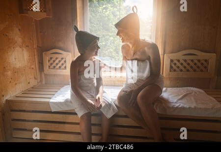 Mutter und Tochter genießen einen Saunagang, tragen Filzhüte und in Handtücher gewickelt Stockfoto