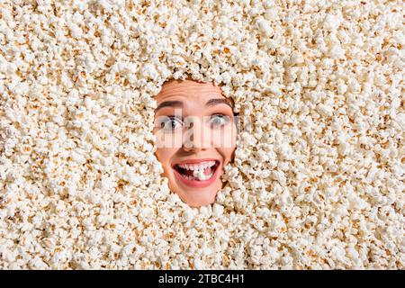 Oben sehen Sie ein Foto des fröhlich erstaunten überglückten Mädchengesichts, das isoliert auf dem Hintergrund mit vollem Popcorn begraben wurde Stockfoto