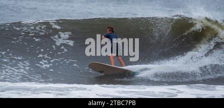 Gilgo Beach, New York, USA - 31. August 2023: Ein Mann, der im Regen auf einer großen Welle auf einem Surfbrett reitet. Stockfoto