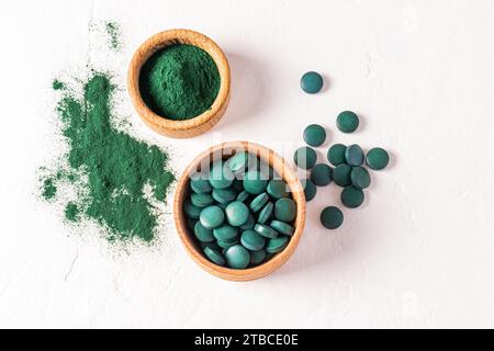 Zwei hölzerne Schalen mit Tabletten und Puder grüner natürlicher Spirulina-Algen auf weißem texturiertem Hintergrund. Draufsicht. Superfood. Entgiftung Stockfoto