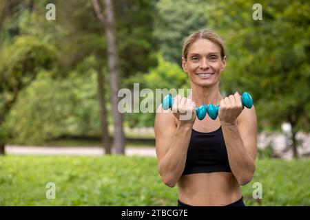 Sportliche Frau, die Hände mit Kurzhanteln trainiert, hat Training im Park. Stockfoto