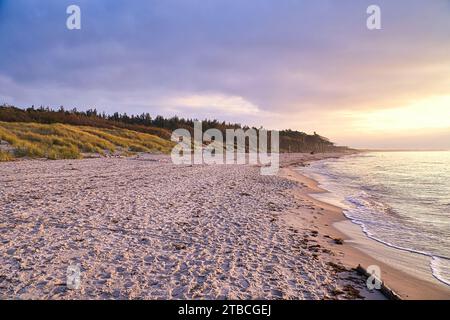 Sonnenuntergang am Weststrand an der Ostsee. Wellen, Strand, bewölkter Himmel und die letzten Sonnenstrahlen an der Küste. Querformat Stockfoto