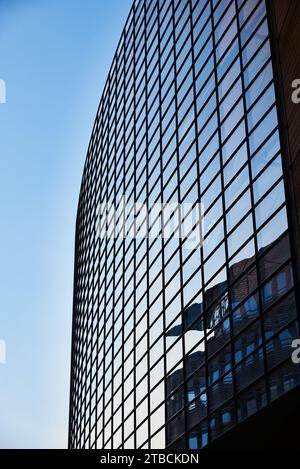 Verglaste moderne Bürofassade vor einem klaren Himmel, der sich auf der verglasten Fassade des Gebäudes spiegelt. Schöne moderne Fassade für Geschäftsleute oder Hauptsitz in Berlin Stockfoto