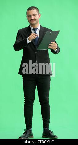Junger Mann in vollem Wachstum. Isoliert auf grünem Hintergrund, wenn man sich den Papierbericht ansieht Stockfoto