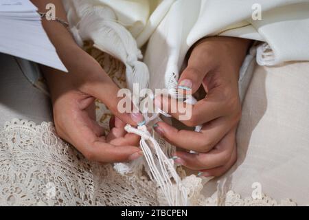 Eine Frau mit nagellack sammelt den Zitzit, die vier geknüpften Saitenecken des Tallit-Gebetschals, während sie morgens das Schema yisrael rezitiert Stockfoto