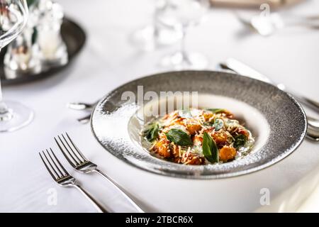 Gnocchi Pomodoro mit Mascarpone, Creme, Basilikum und Parmesan auf einem stilvollen Teller auf einem Restauranttisch. Stockfoto